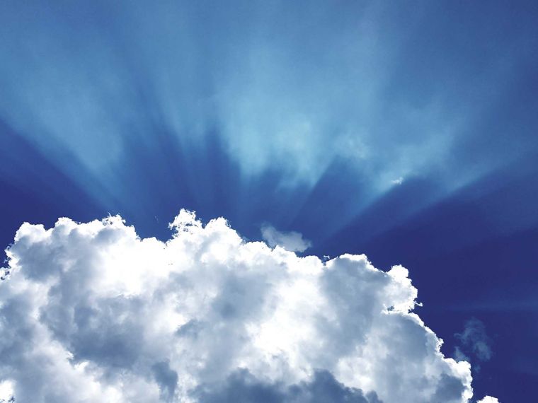 Rays of light appearing from behind a cloud with blue sky.